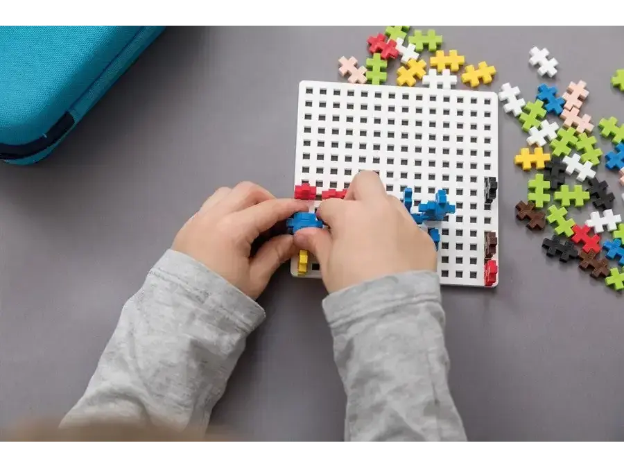 Pegboard with colorful plastic pieces being inserted by hands.