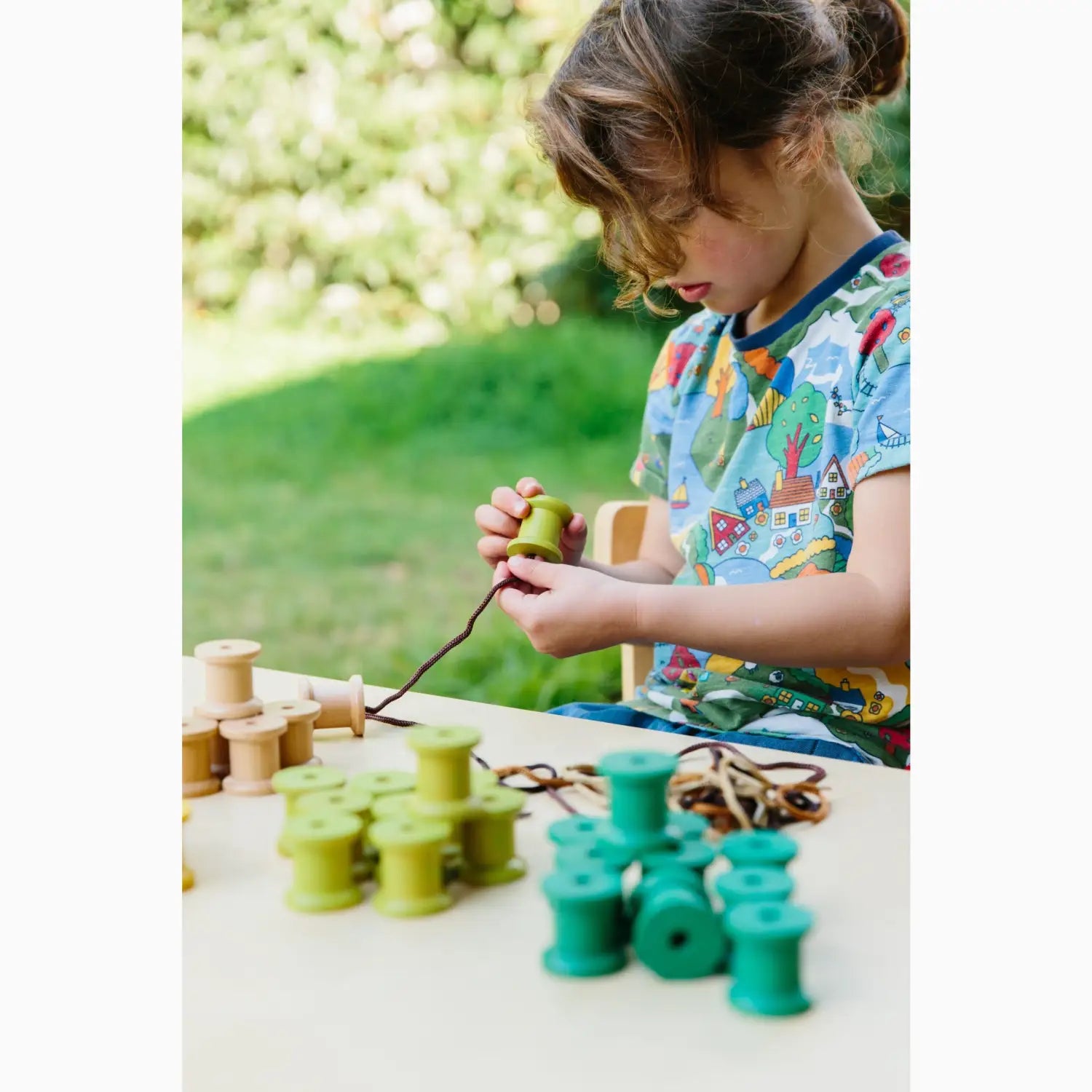 Child engaged in a craft activity with spools and string outdoors.