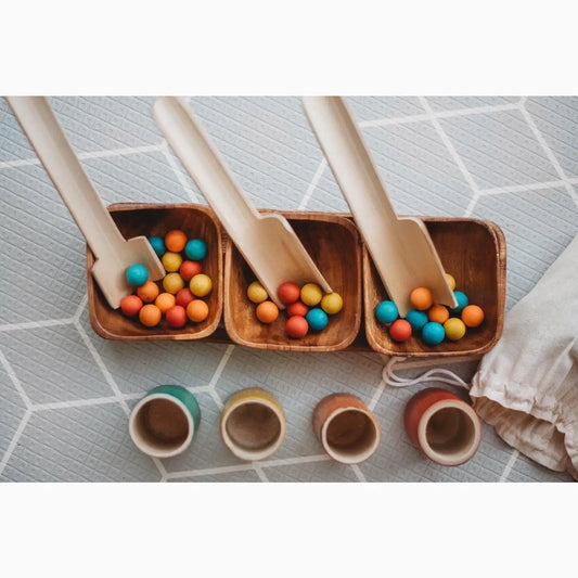 Wooden trays filled with colorful wooden balls alongside small ceramic cups.