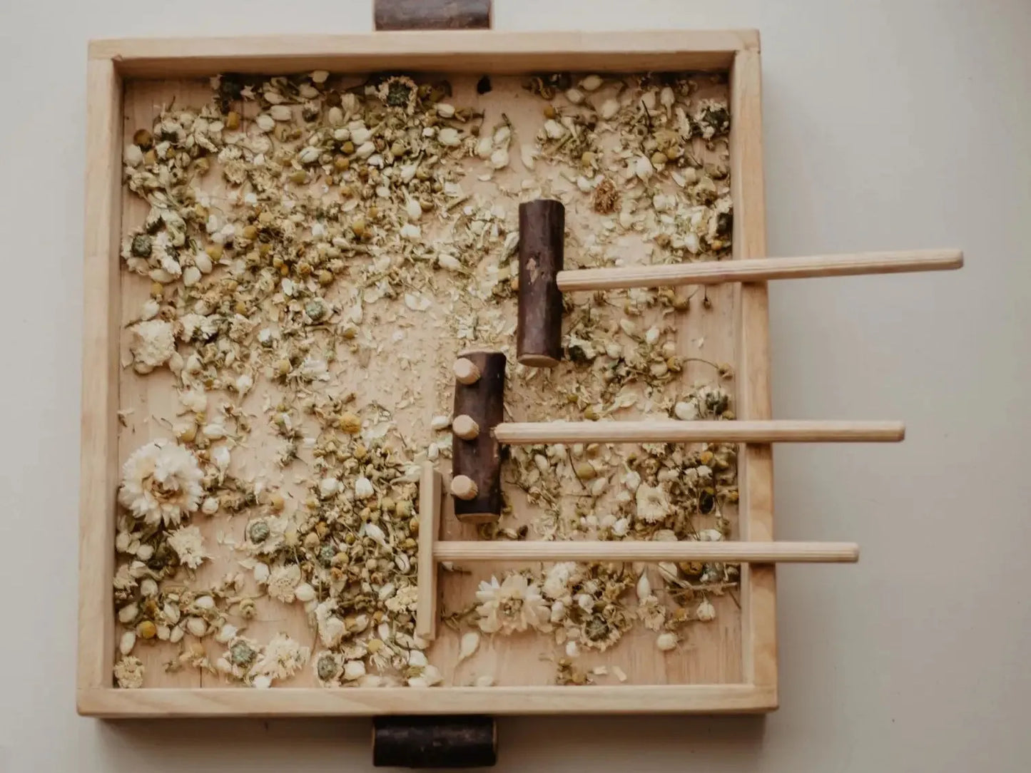 Wooden tray filled with crushed herbs and wooden sticks arranged in a pattern.