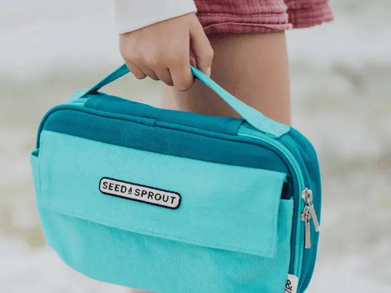 Teal-colored insulated lunch bag with ’SEED & SPROUT’ branding being carried by a hand.