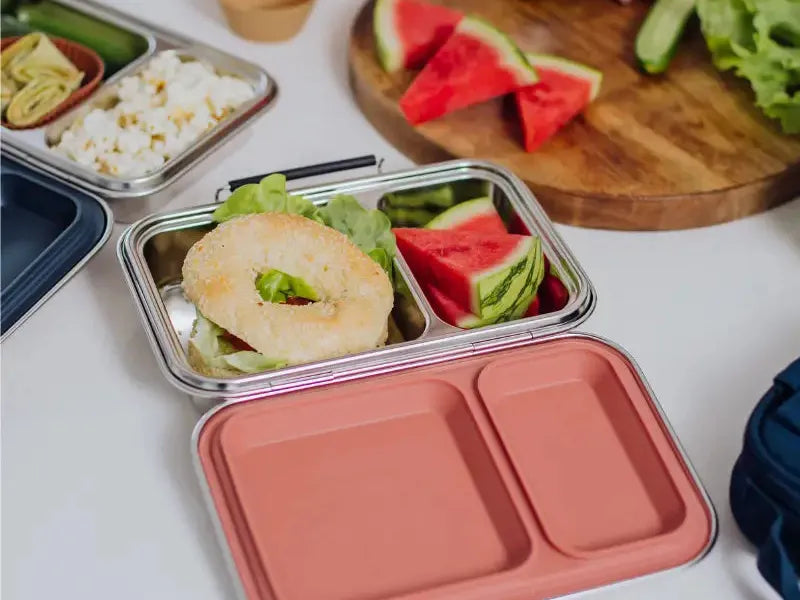 Compartmentalized lunch containers filled with various foods like sandwiches, watermelon, and rice.