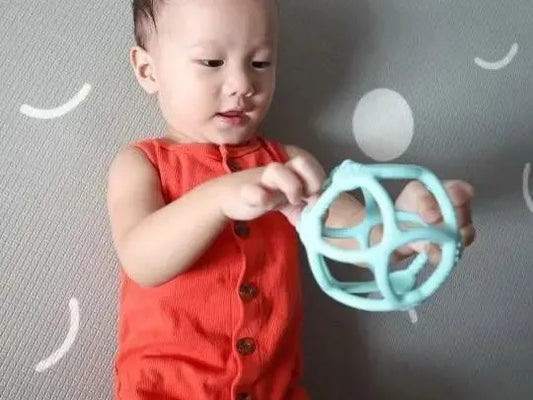 Baby in a red sleeveless outfit holding a light blue teething toy.