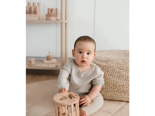 Baby sitting on the floor playing with a wooden toy.