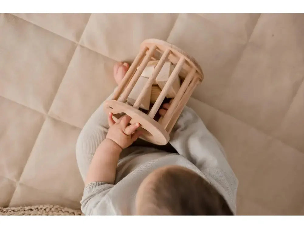 Wooden cylindrical cage or rattle held by small hands.