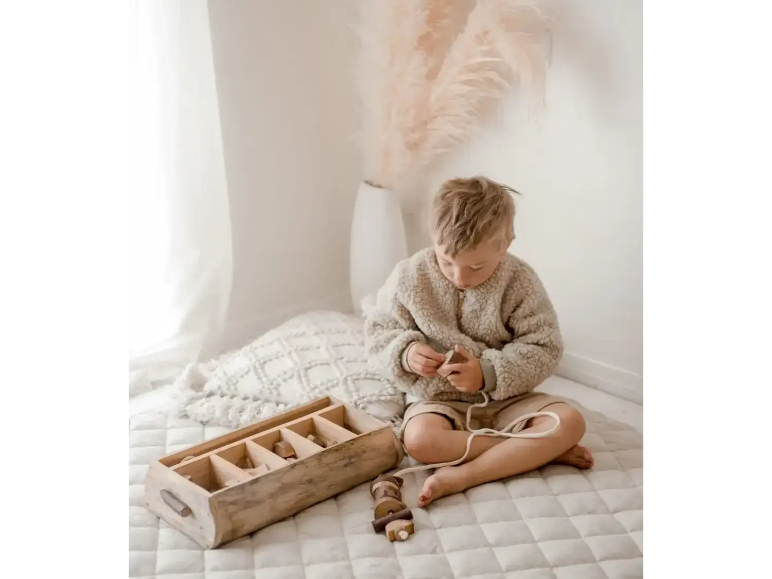 Child sitting cross-legged on a quilted surface, wearing a cozy sweater.