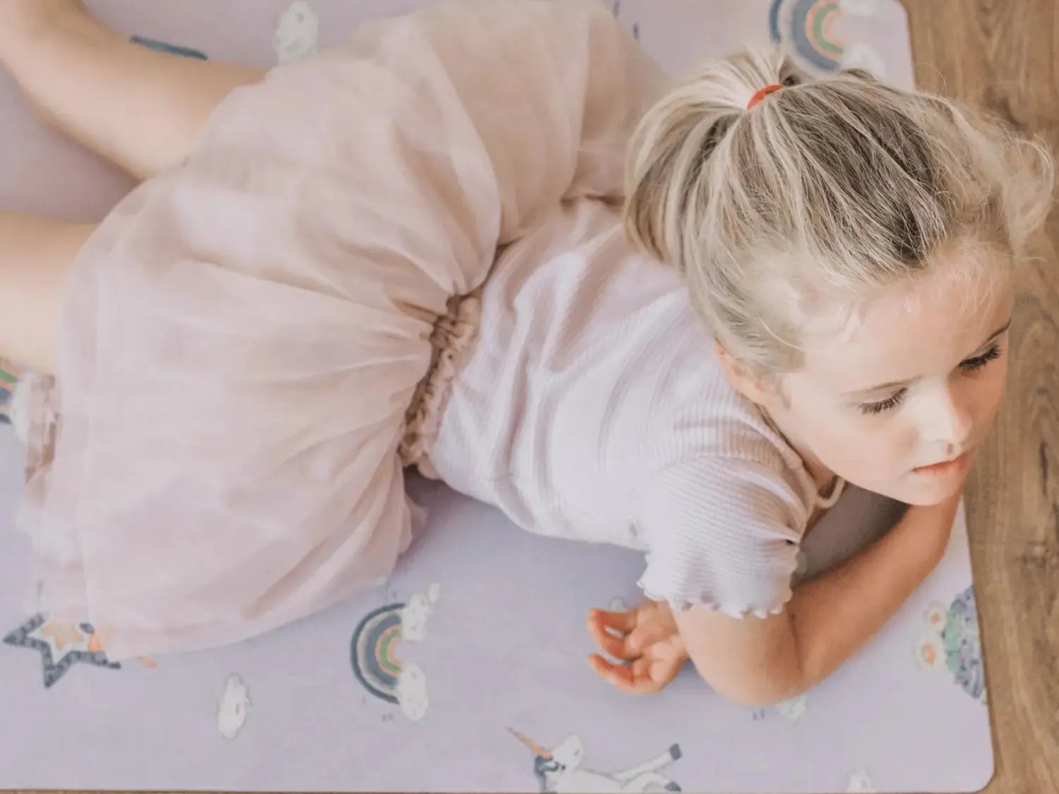Young girl in a pale pink dress lying on a patterned play mat.