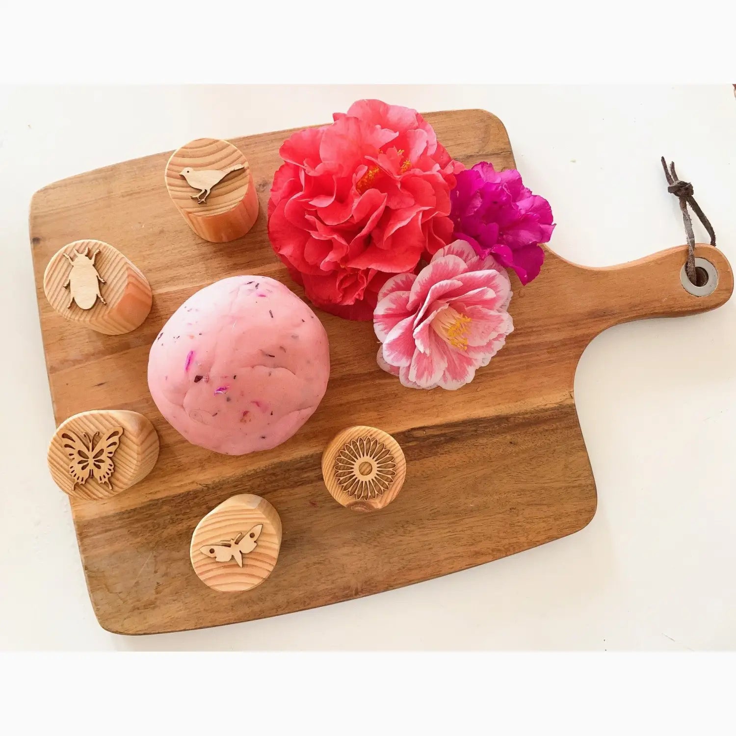 Wooden cutting board with flowers, a pink sphere, and decorative wooden stamps.