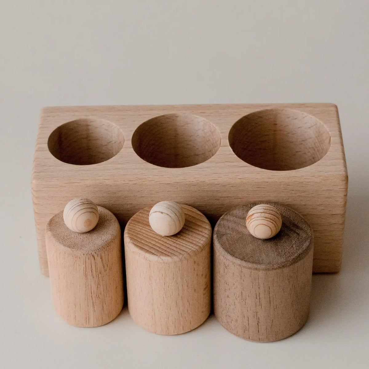 Wooden toy or educational tool with three cylindrical pieces fitting into corresponding holes.