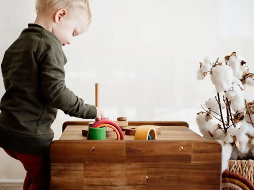 Wooden toy box or activity table with colorful shapes and objects on top.
