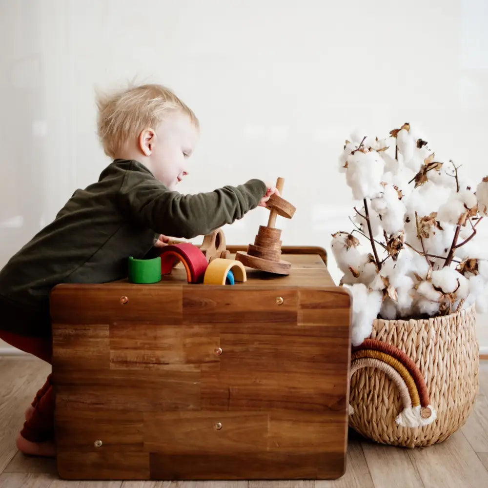 Young child playing with wooden toys on a wooden chest.