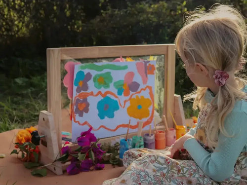 Colorful painting on an easel being created by a young child outdoors.