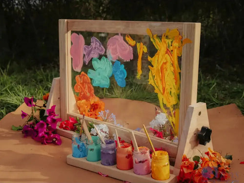 Colorful paint-splattered wooden frame with jars of paint and flowers arranged around it.