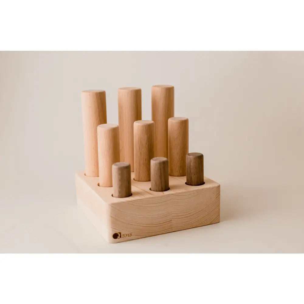 Wooden block with cylindrical pegs of varying heights inserted into holes.