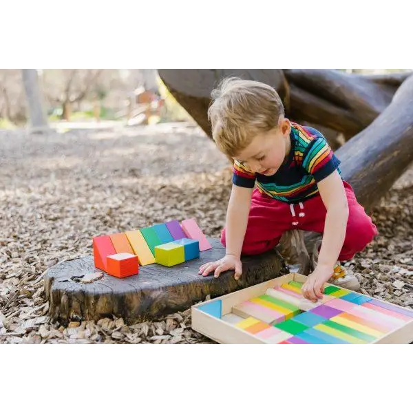 Child playing with colorful wooden blocks on a tree stump.