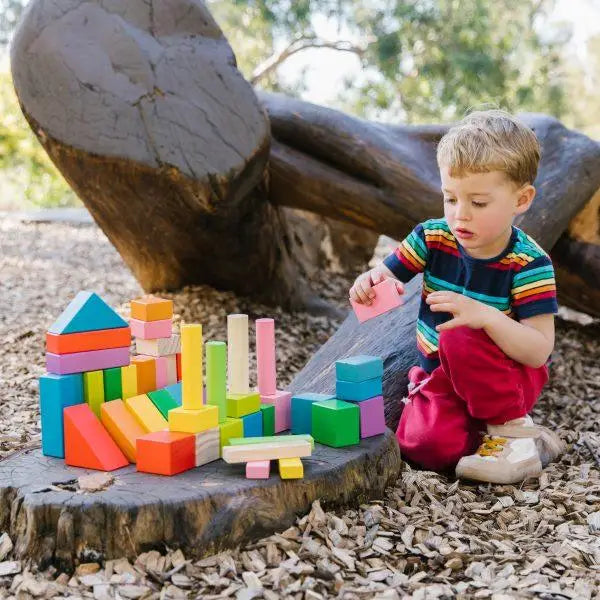 Young child playing with colorful wooden building blocks outdoors.