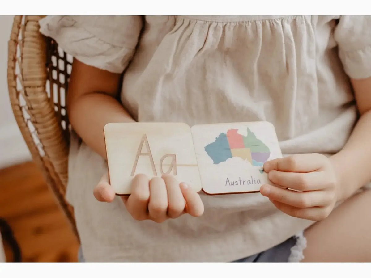 Wooden educational card or block with the letter ’A’ and colorful cloud shapes held by small hands.