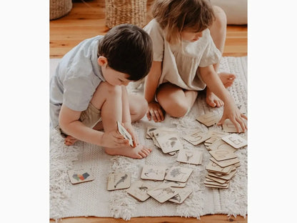 Two children sitting on a rug playing with cards or small paper items spread out in front of them.