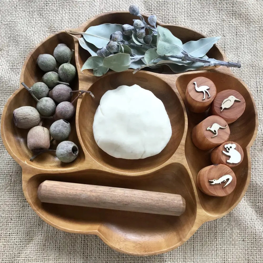 Wooden tray with compartments containing various natural objects and play materials.