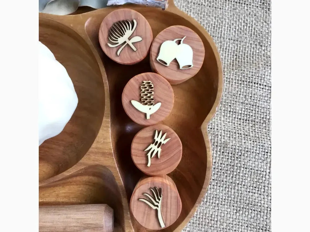 Wooden palette-shaped board with circular indentations containing small white decorative objects.