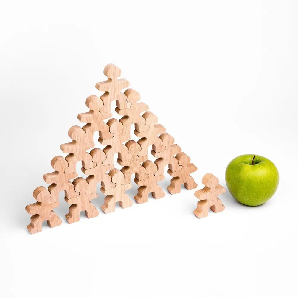 Triangular stack of wooden human-shaped figures with one figure separate and a green apple beside it.