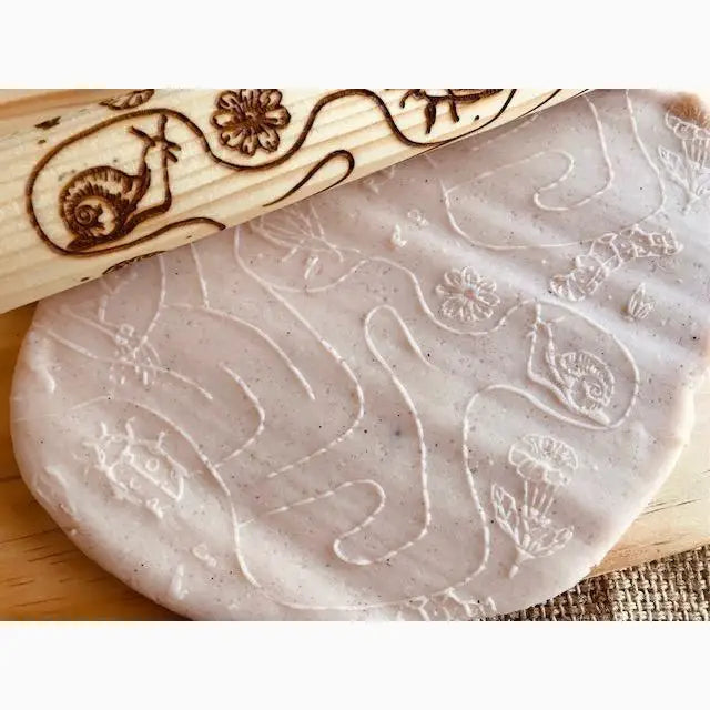 Clay or dough imprinted with a decorative rolling pin featuring snail and flower designs.