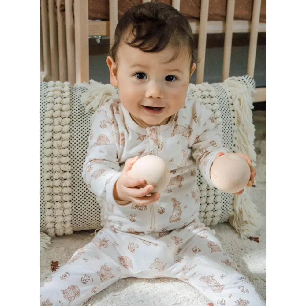 Baby in a patterned onesie holding two round objects.