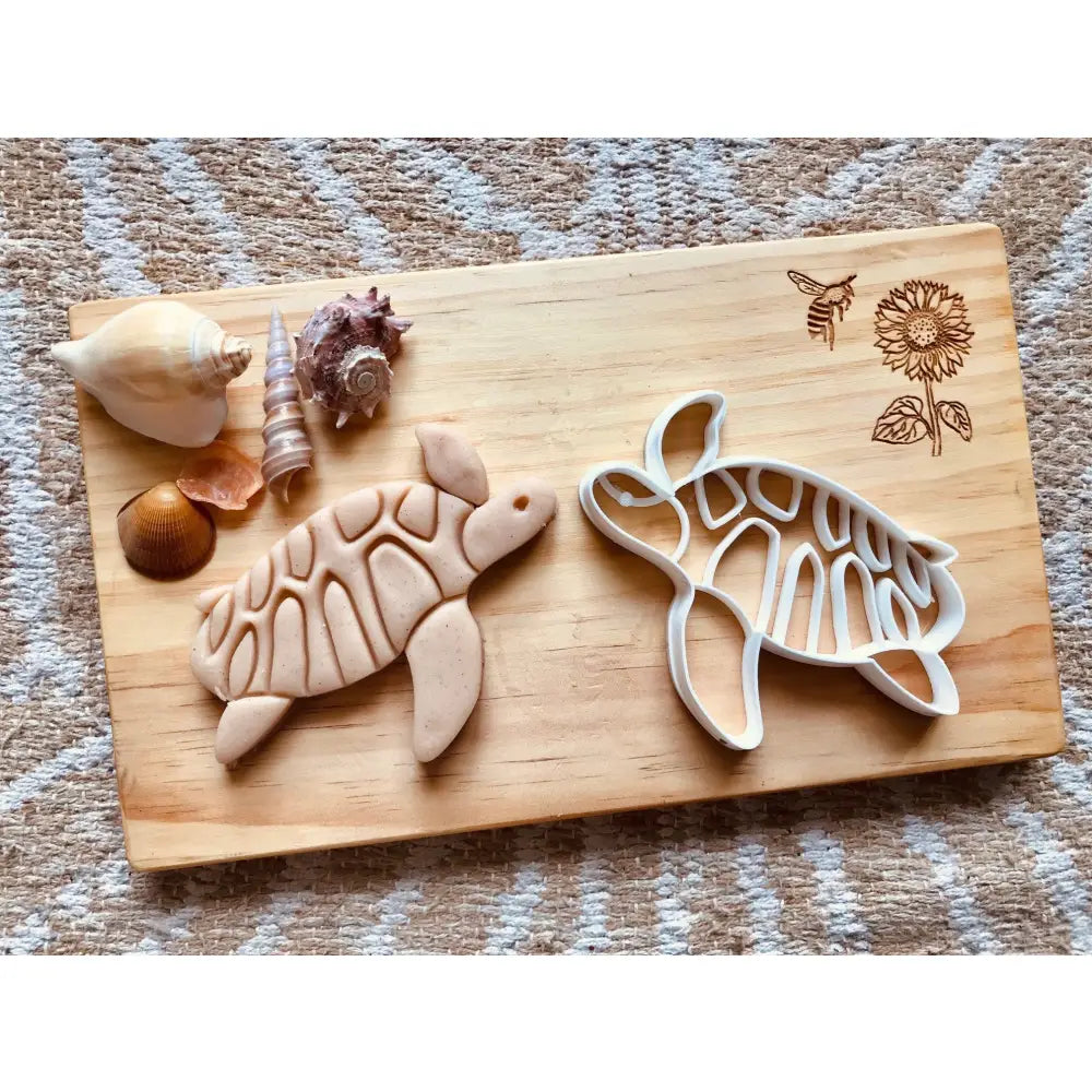 Wooden cutting board with turtle-shaped cookie cutters and seashells.