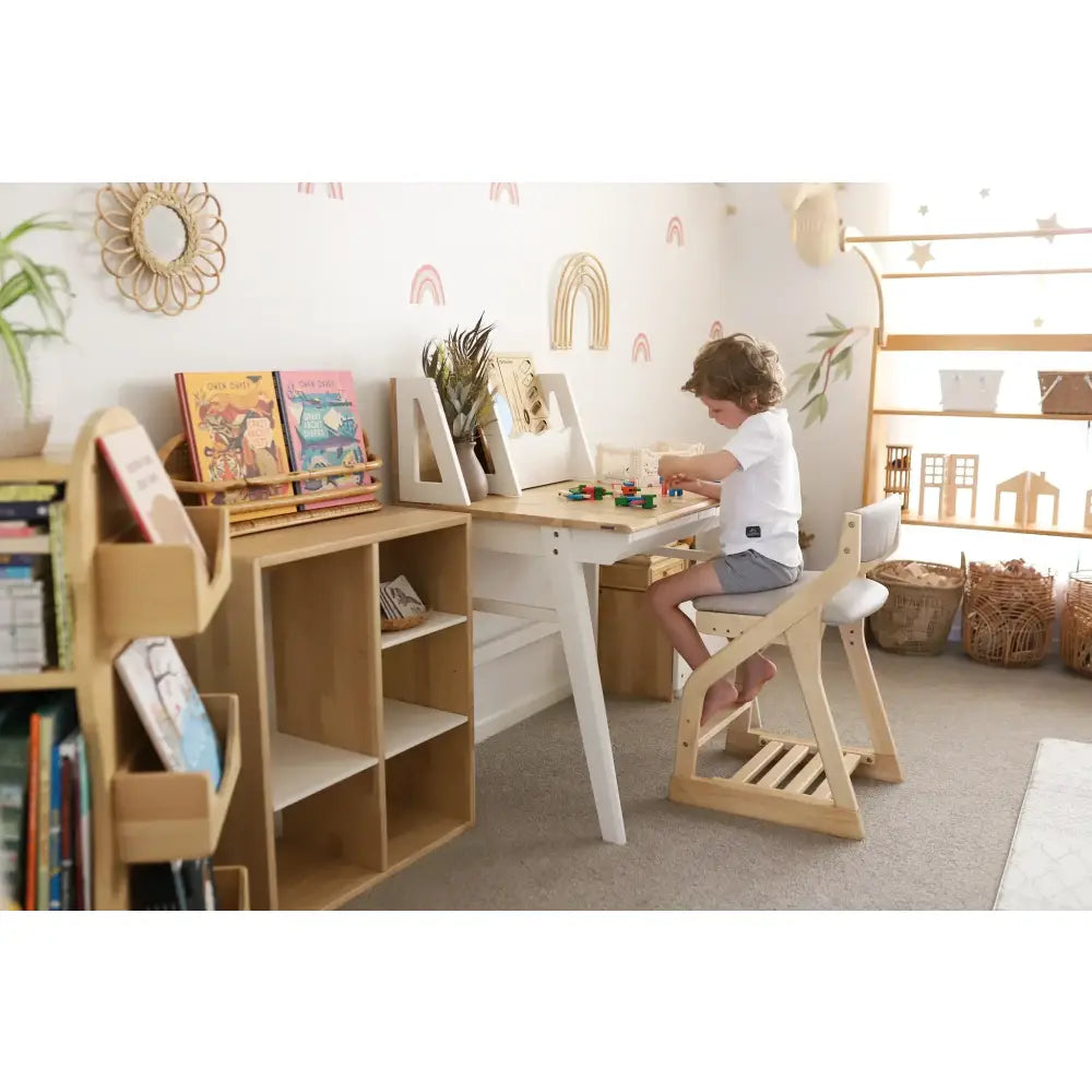 Child sitting at a wooden desk in a playroom or bedroom.