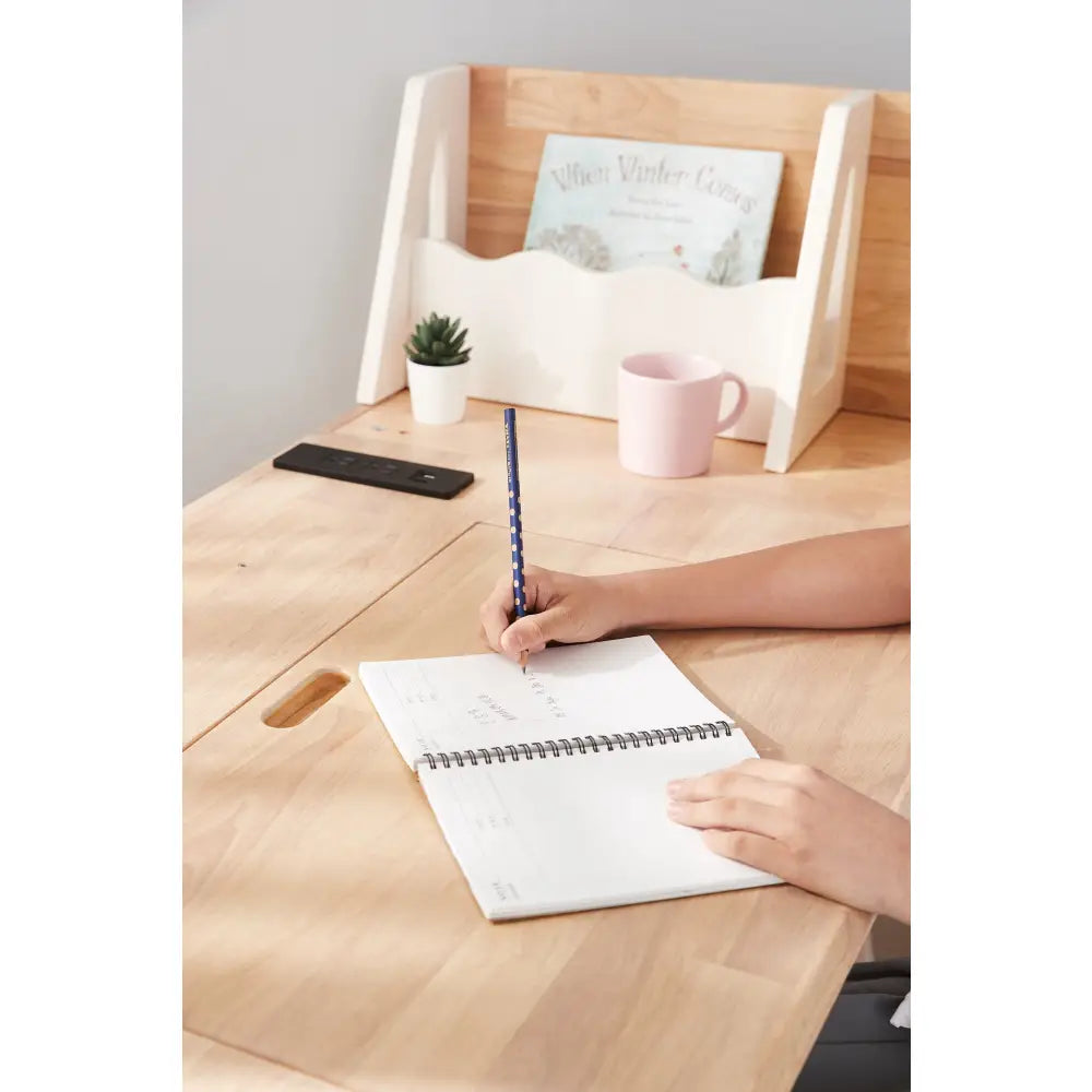 Wooden desk or table with a person’s hands writing in a notebook.