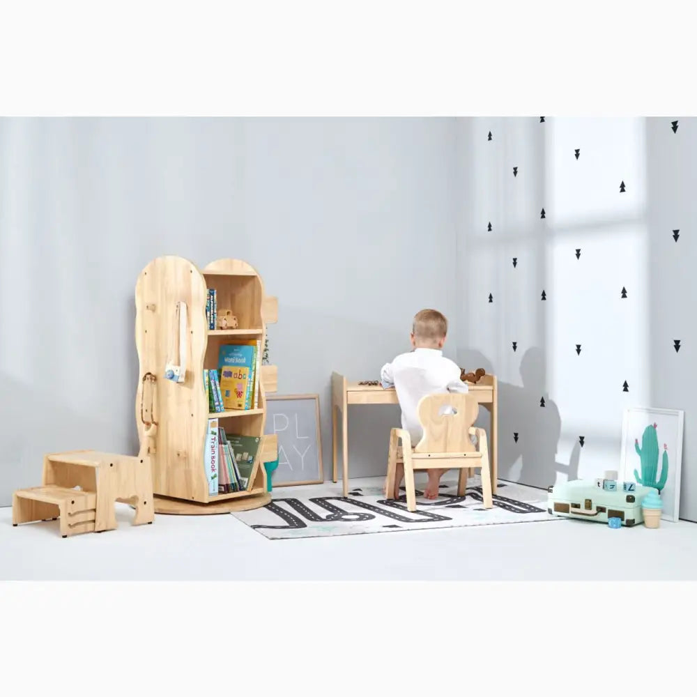 Child sitting at a small wooden desk in a minimalist playroom setting.