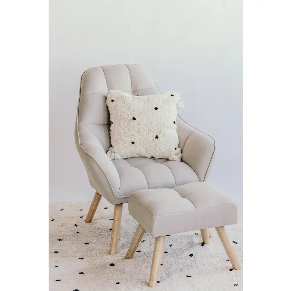 Beige upholstered armchair with matching footstool and decorative pillow.