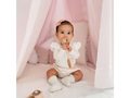 Baby wearing a white outfit sitting on a soft surface.