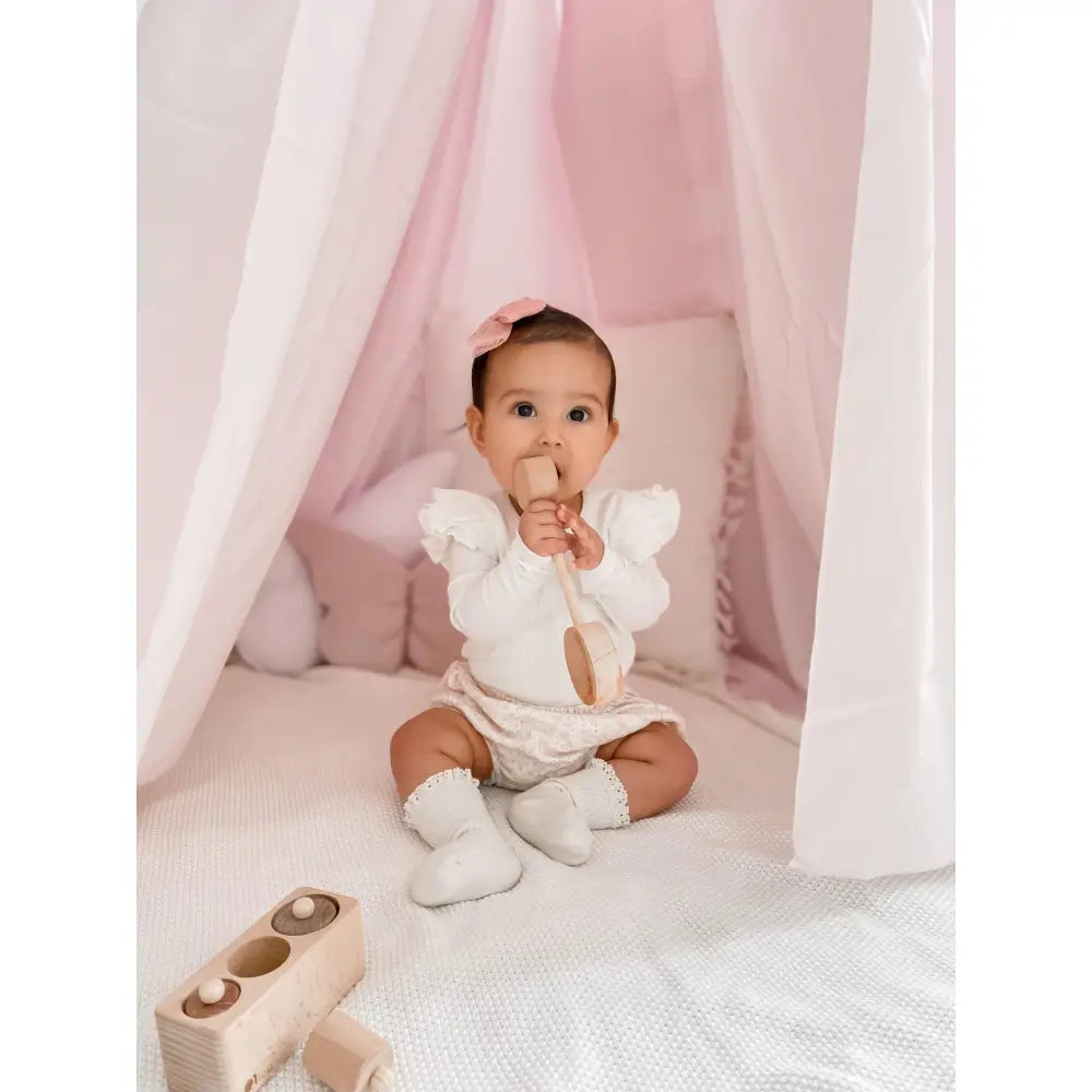 Baby wearing a white outfit sitting on a soft surface.