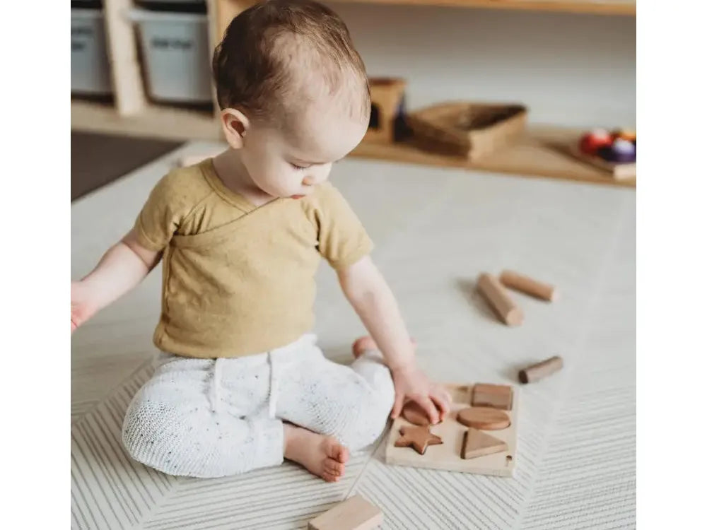 Baby sitting on the floor playing with wooden blocks.