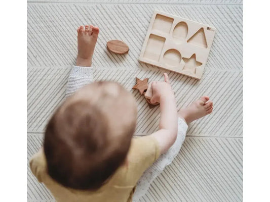 Baby playing with wooden shape sorting toy on a textured surface.