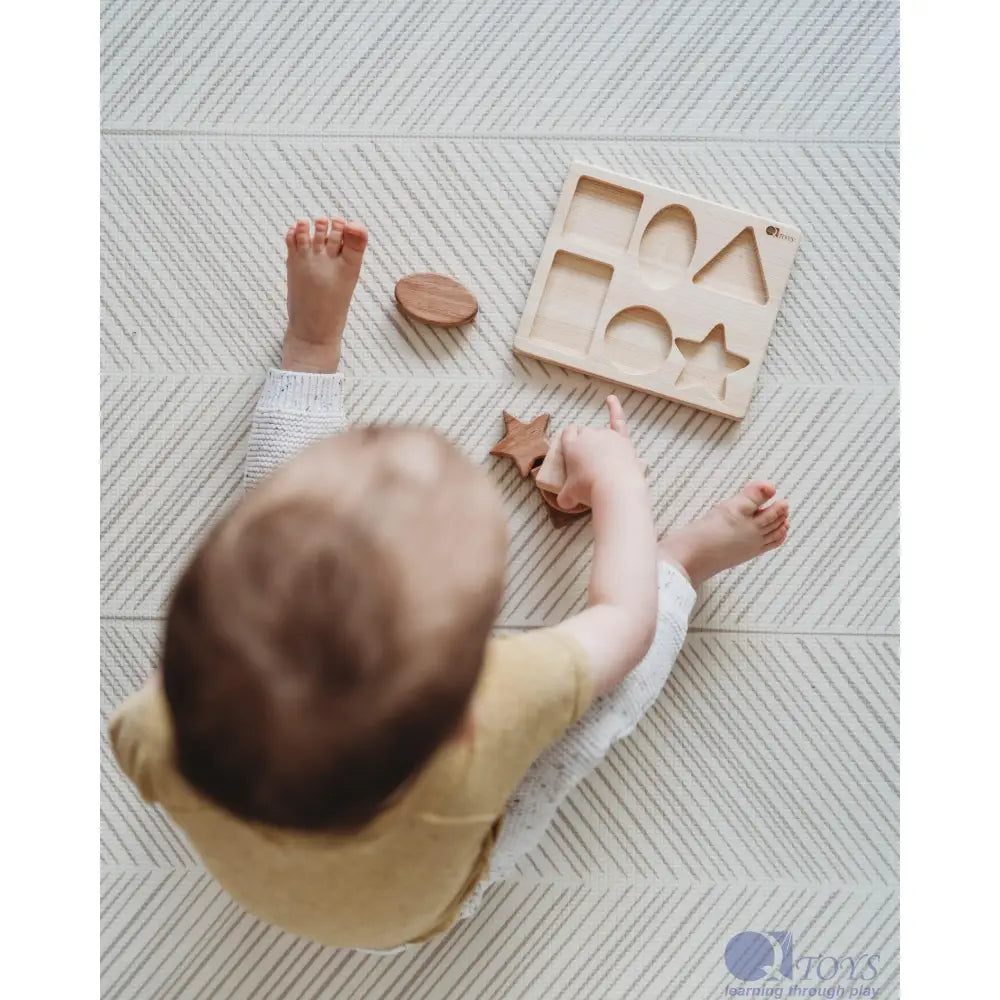 Baby playing with wooden shape sorting toy on a textured surface.