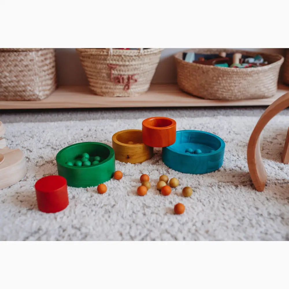 Colorful stacking rings toy with small wooden balls scattered around it.