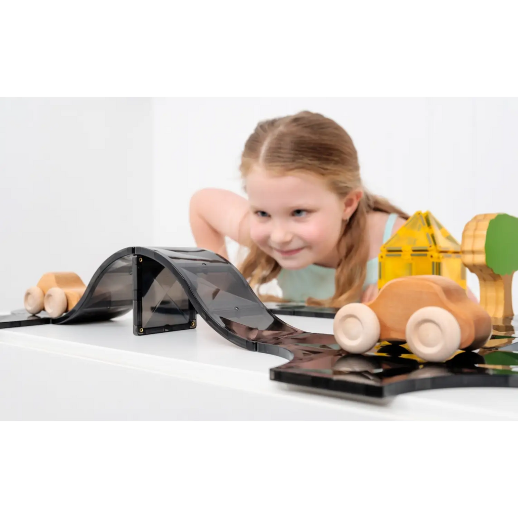 Young child playing with wooden toy vehicles and a toy road or track.