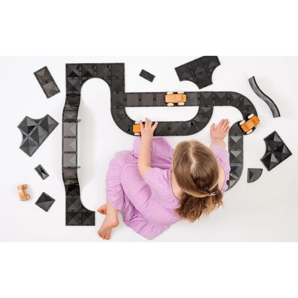 Child in a purple shirt playing with a toy car track on a white surface.