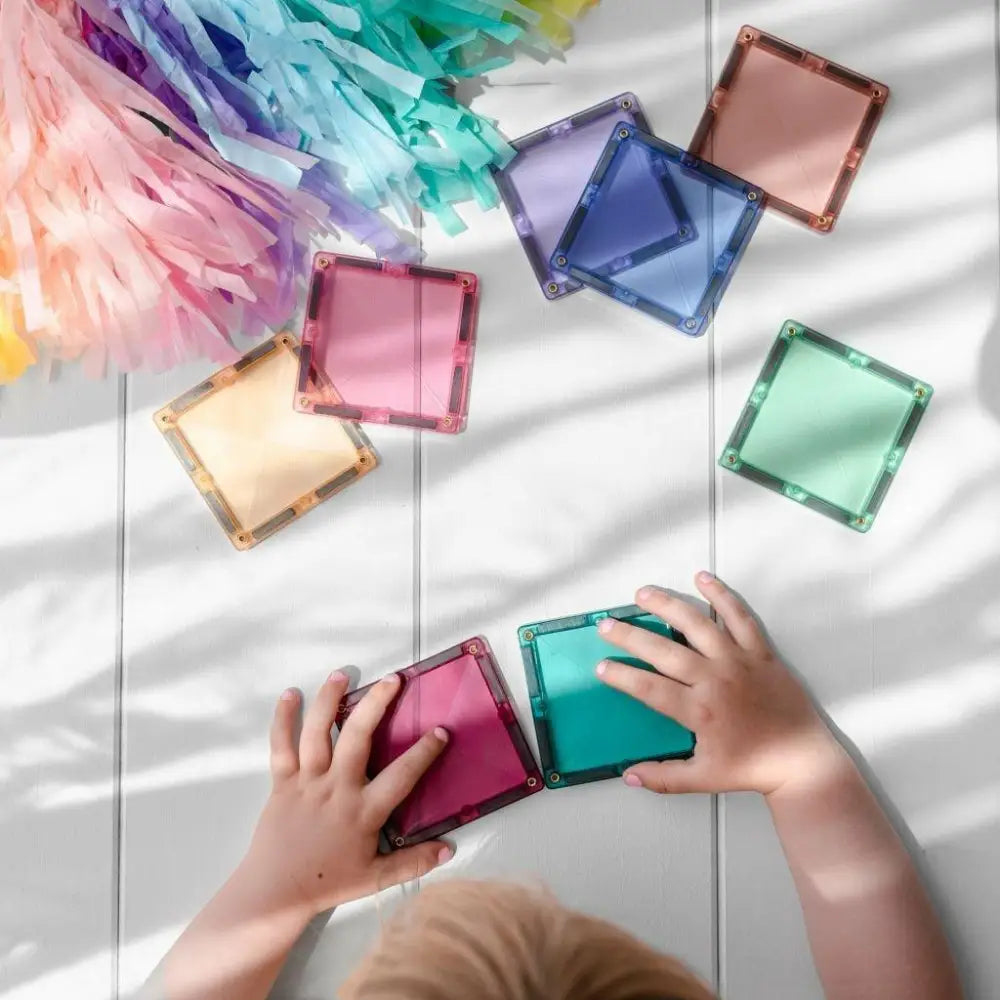 Colorful square magnetic tiles being arranged by a child’s hands.