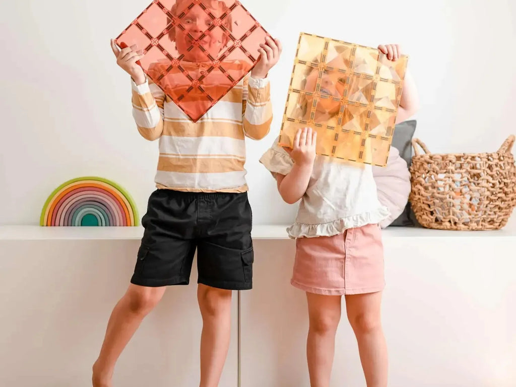 Two children holding colorful geometric tiles in front of their faces.
