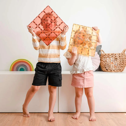 Two children holding colorful geometric tiles in front of their faces.