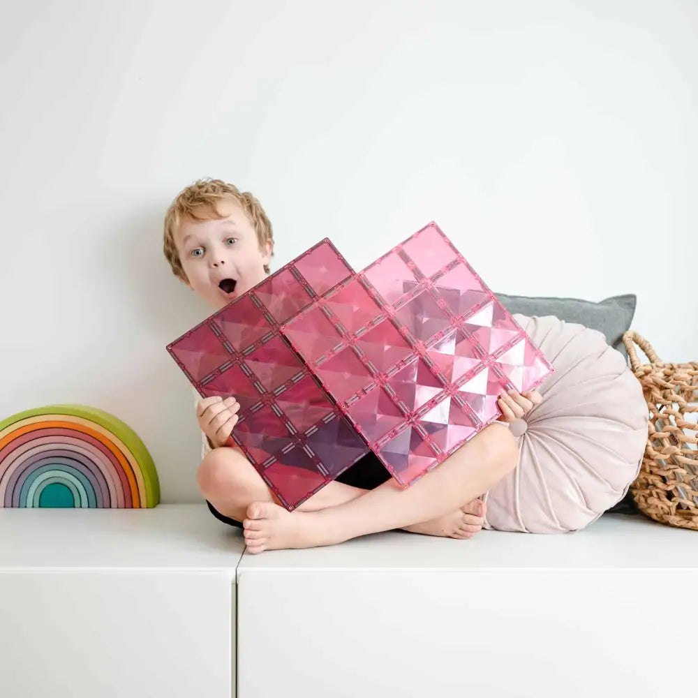 Young child holding a pink geometric cushion with a surprised expression.