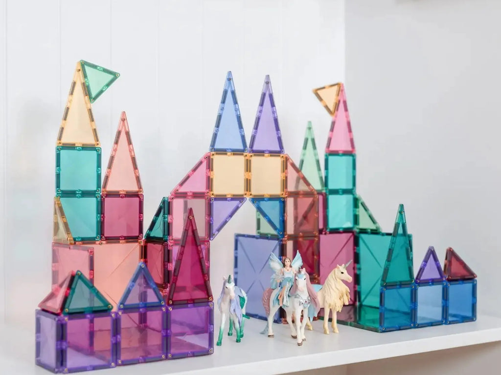 Colorful magnetic building tiles arranged into a castle-like structure with toy unicorn figures in front.