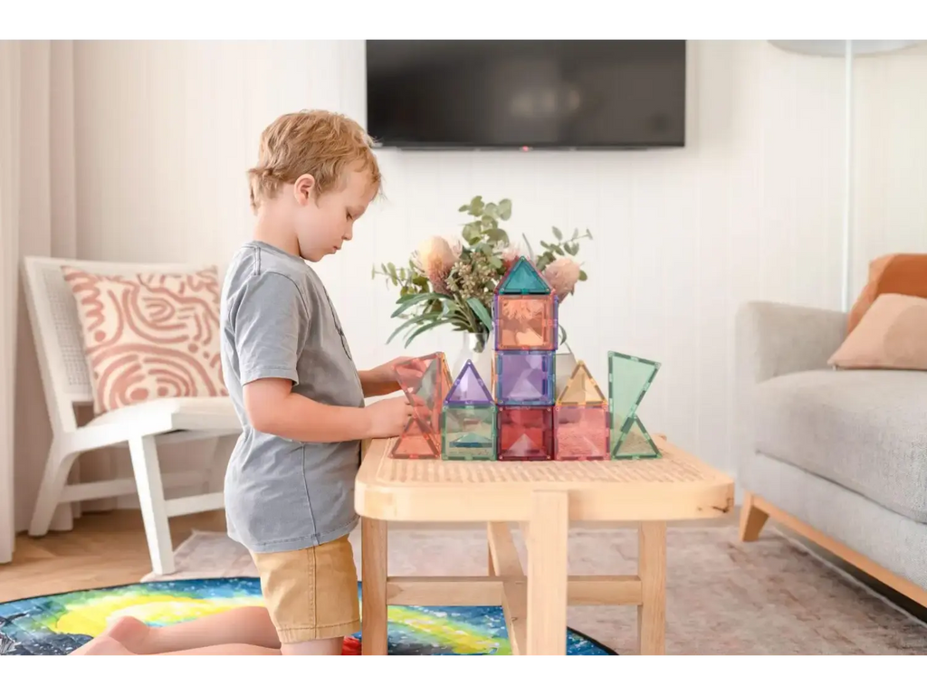 Child playing with colorful magnetic building tiles on a wooden table.