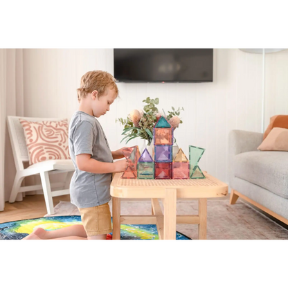 Child playing with colorful magnetic building tiles on a wooden table.
