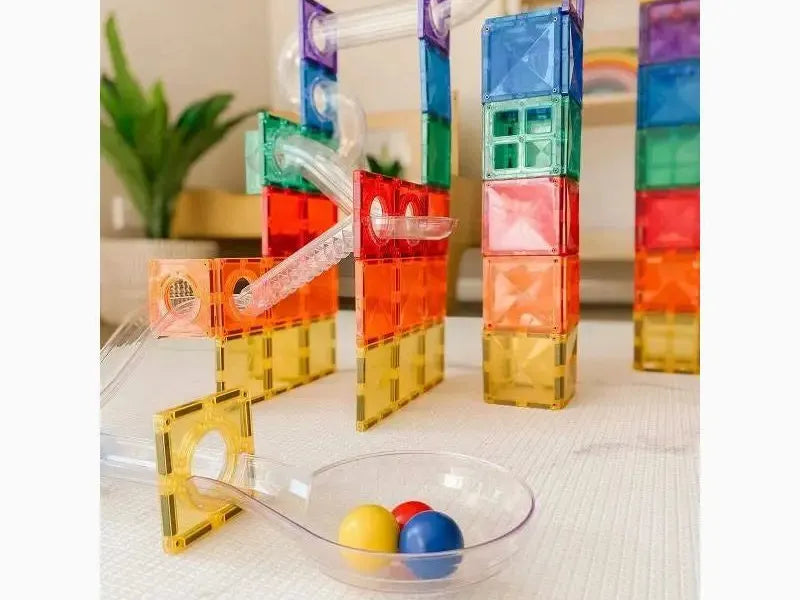 Colorful magnetic building tiles arranged in tower-like structures with a small ramp and bowl of spheres.