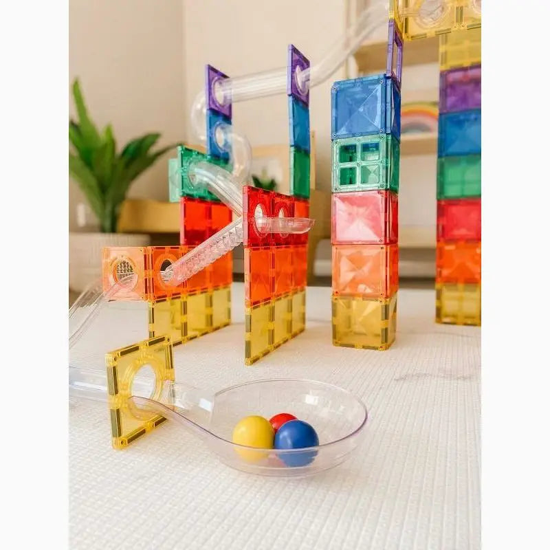 Colorful magnetic building tiles arranged in tower-like structures with a small ramp and bowl of spheres.