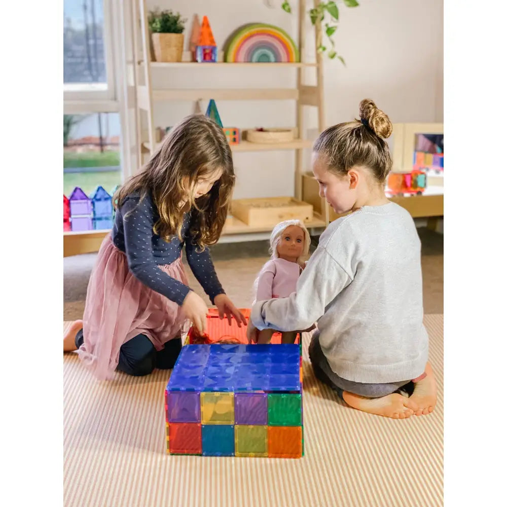 Two children playing with colorful building blocks on a carpeted floor.